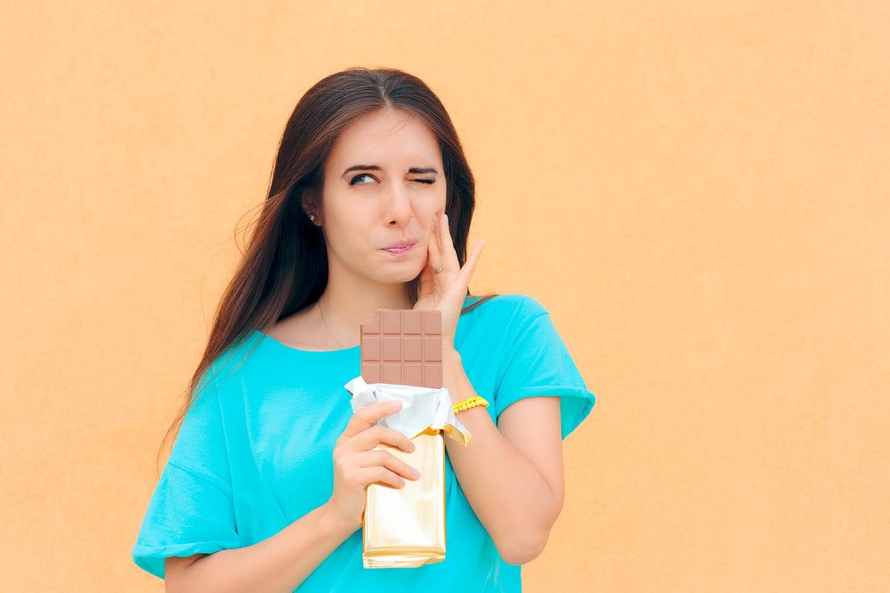 Stock image of girl touching painful tooth. with chocolate in her hand