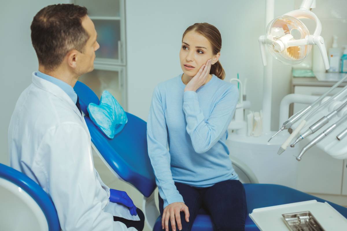 Young woman speaking with dentist due to tooth pain.